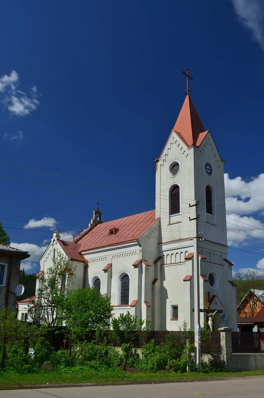 Білий костел з високою вежею й червоним шпилем на тлі синього неба