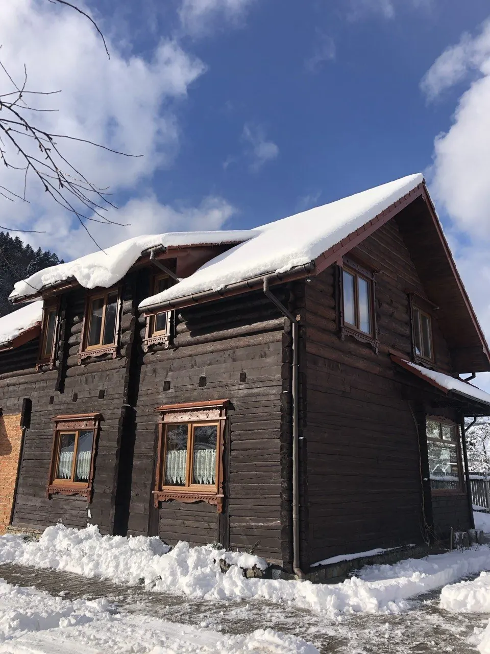 Дерев'яна двоповерхова хата зі снігом на даху й біля стін, блакитне небо з хмарами