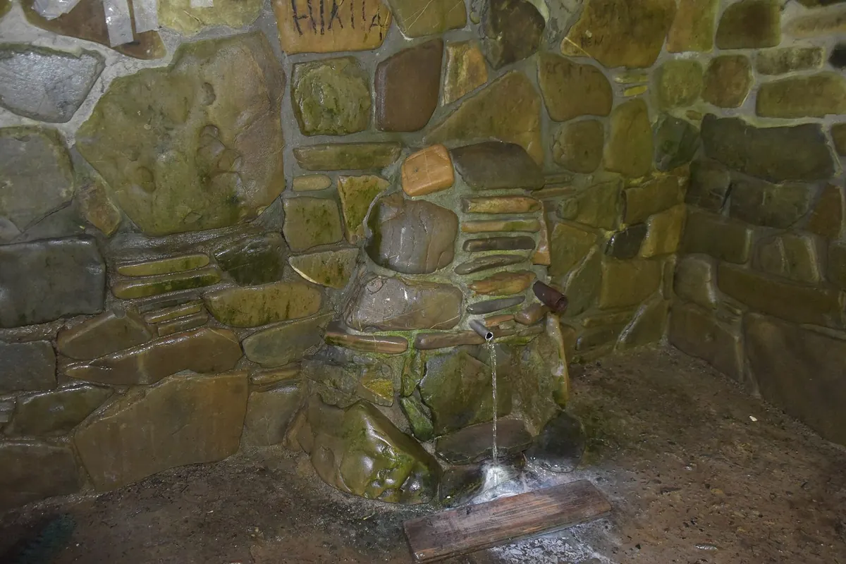 Джерело в кам'яній кладці, вкритій мохом: з трубки тече вода на дерев'яну дошку