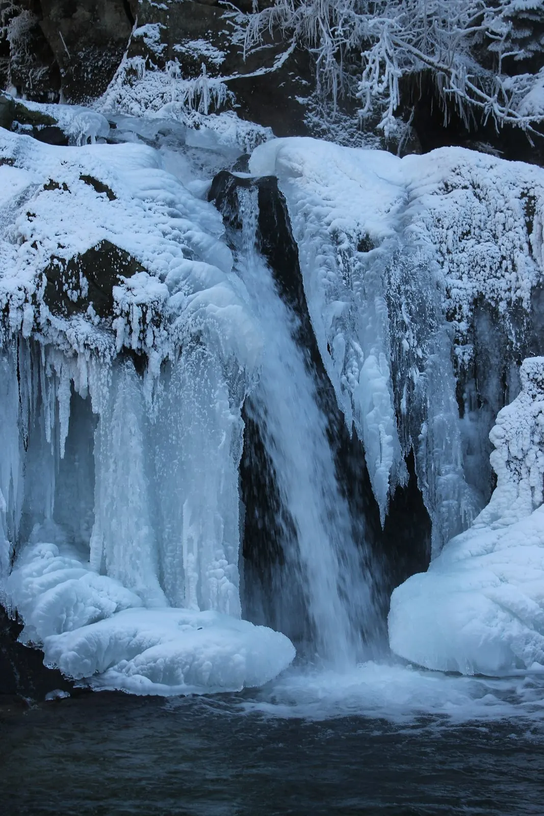 Вузький струмінь води між крижаними бурульками й засніженими каменями